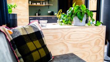 A cozy living area with a sofa, a coffee table, and a kitchen counter with plants and a coffee machine.
