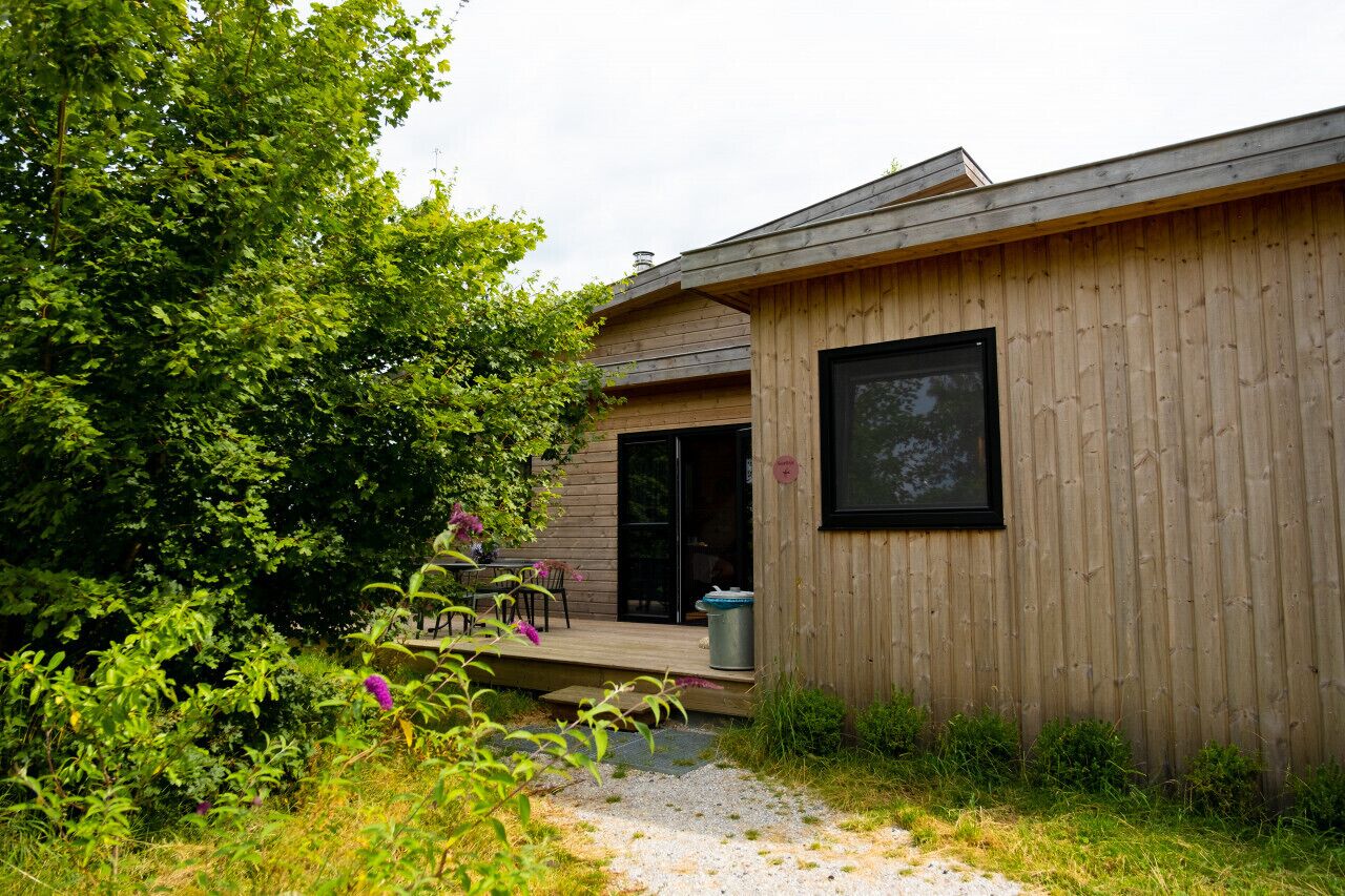 Un bâtiment en bois doté d’une grande fenêtre et d’un espace extérieur abrité, comprenant une table et des chaises.