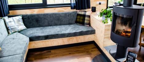 A modern living room with a grey sofa, a wooden side table with a plant, and a wood-burning stove.