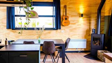A cozy room with a wooden interior, a dining table with chairs, a guitar, and a wood-burning stove.
