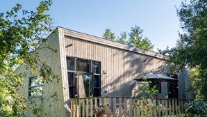 Eine Holzhütte mit einer Terrasse, umgeben von hohem Gras und Bäumen.