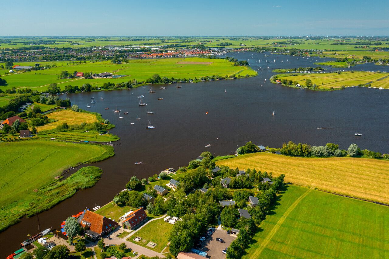 Vista aérea de un pueblo ribereño con barcos, campos verdes y casas a lo largo del agua.