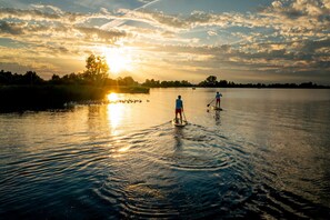 Zwei Personen stehen auf Paddleboards auf einem ruhigen See bei Sonnenuntergang.