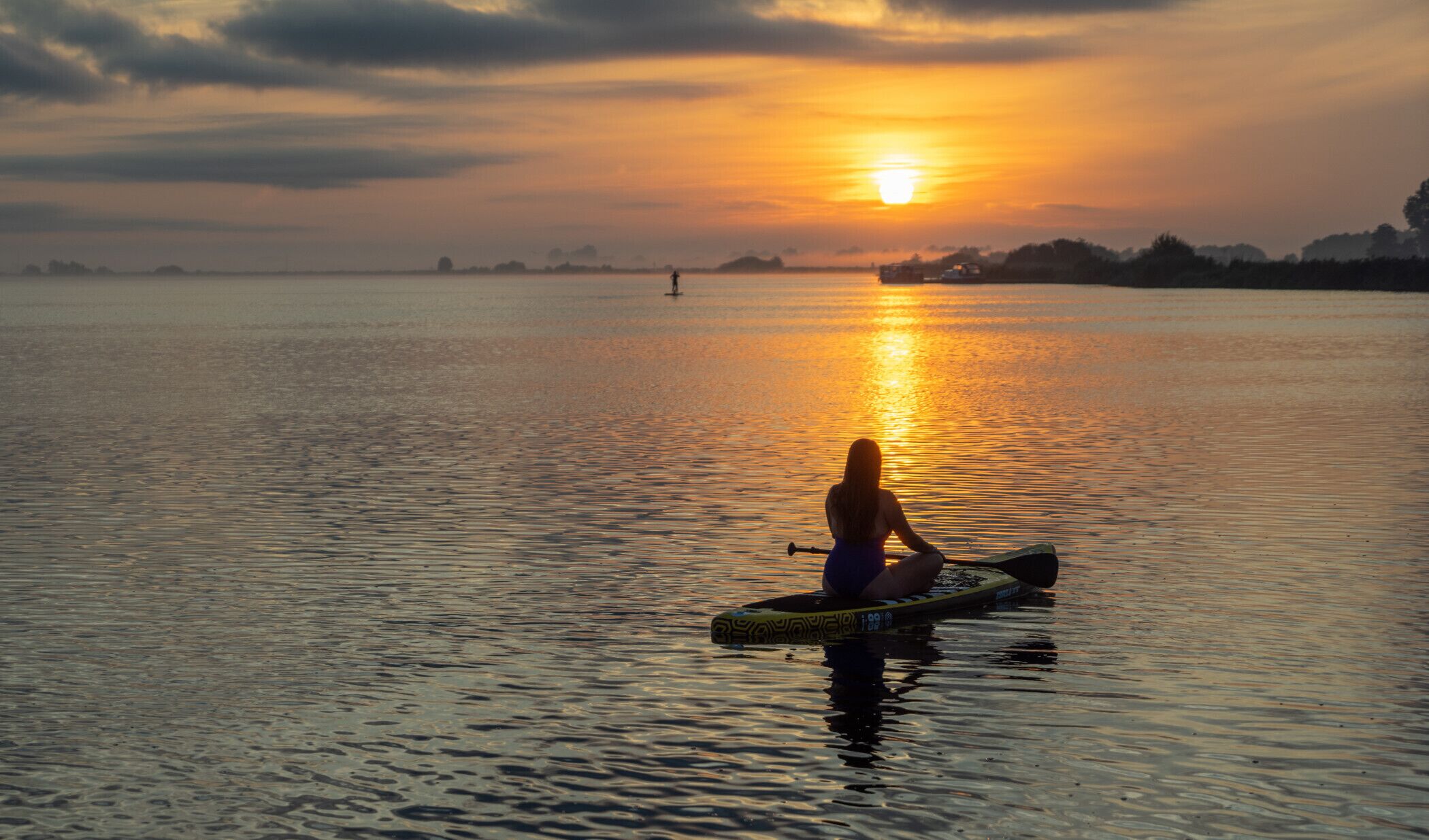 Una persona seduta su una tavola da paddleboard in acque calme al tramonto.