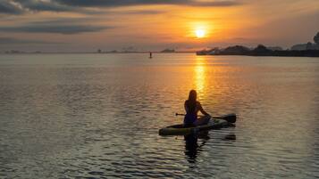 Una persona seduta su una tavola da paddleboard in acque calme al tramonto.