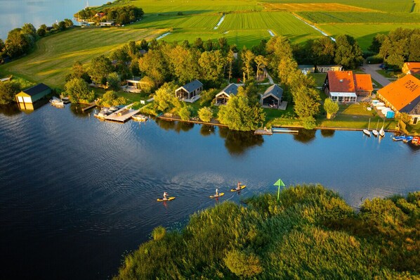 An aerial view of a lakeside property with several houses, a dock, and a boat. - Waterlodge Goudule in Nes (Nes)