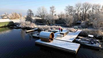 A winter scene with a docked boat, a wooden structure with a barrel, and a small building with a green roof.