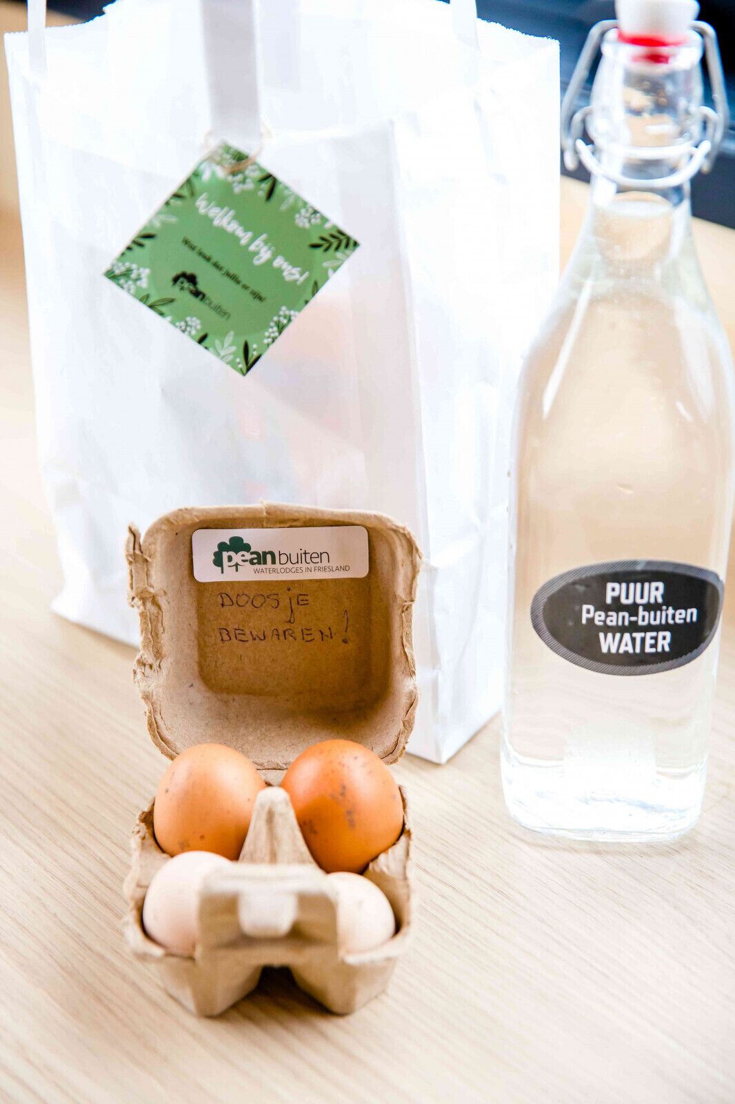 A carton of eggs, a bottle of water, and a white bag with a green label.