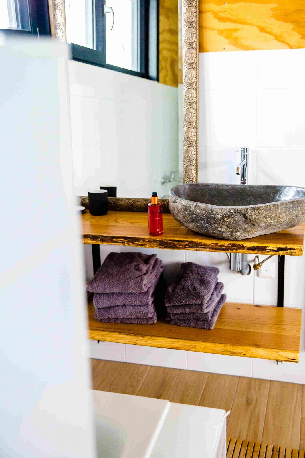 Une salle de bain avec un lavabo en pierre, une bouteille rouge et des serviettes pliées sur une étagère en bois.