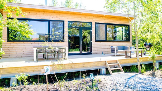 Una casa moderna con ventanas amplias, una terraza, asientos exteriores y una chimenea.