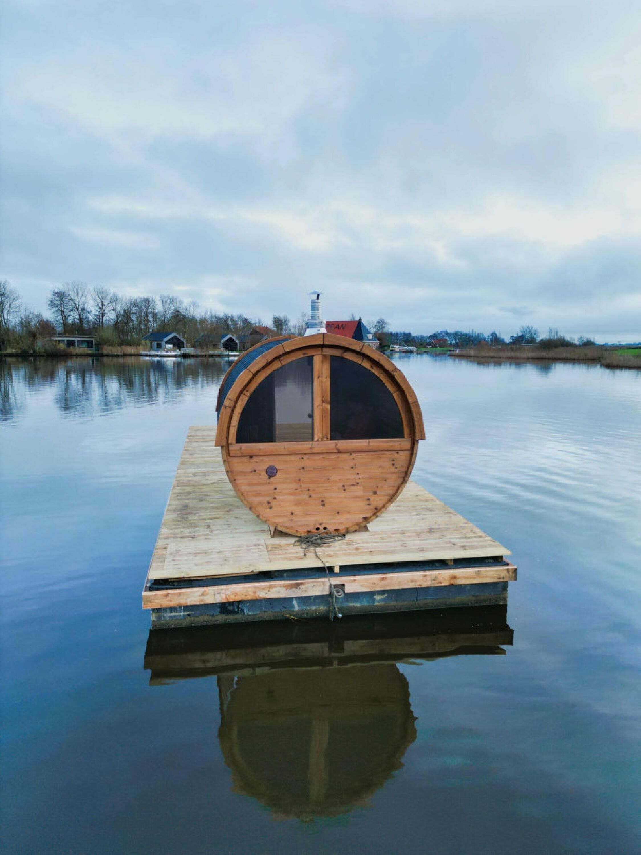A wooden boat house with a round window, docked on a calm body of water.