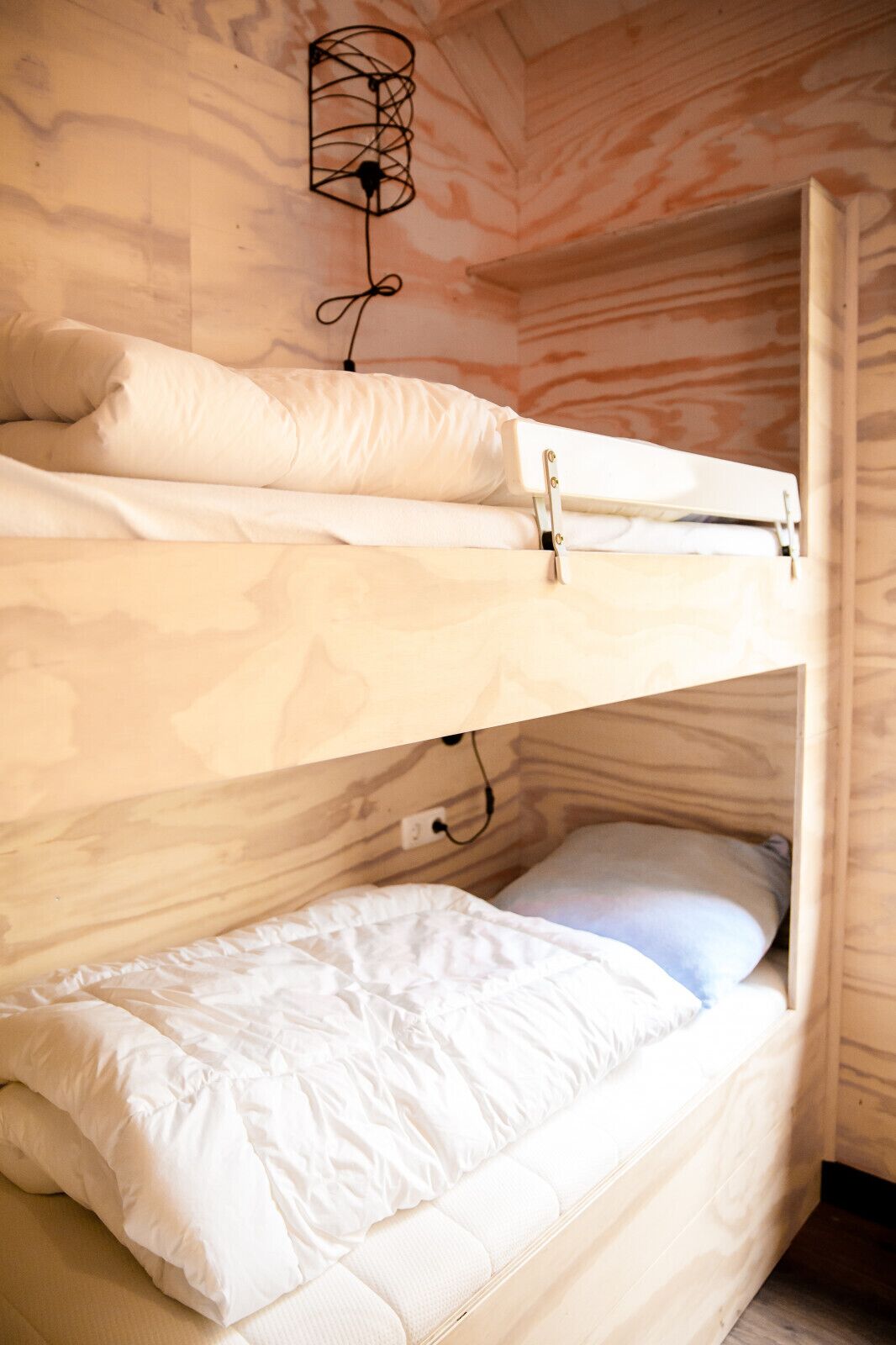 Een stapelbed met witte beddengoed en een wandlamp.
