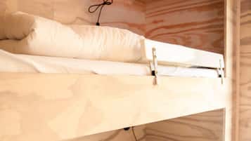 Een stapelbed met witte beddengoed en een wandlamp.