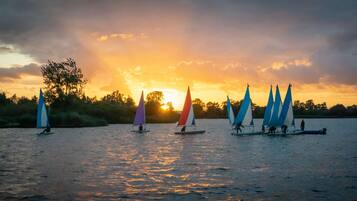 A sunset scene with multiple sailboats on calm water.