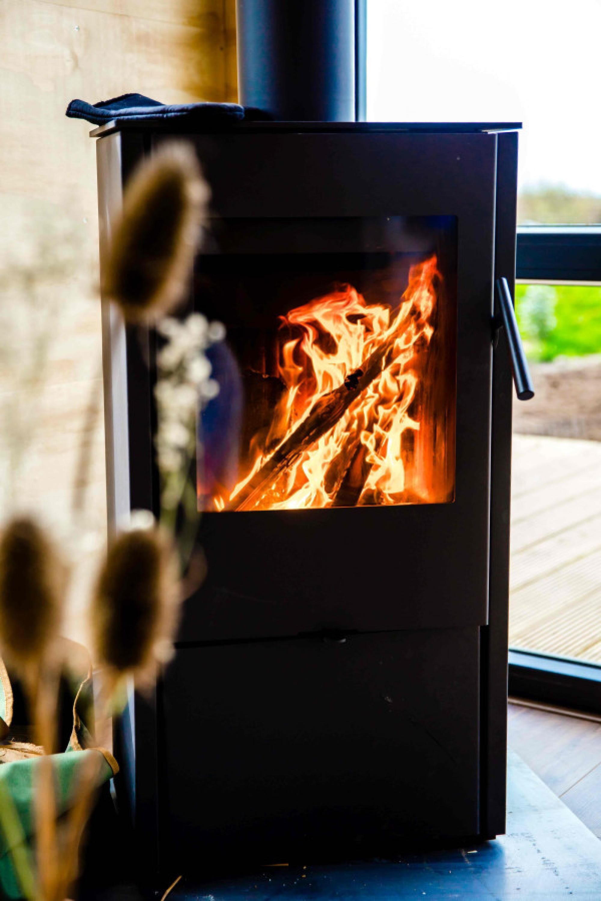 A wood-burning stove with visible flames, a window, and a wooden floor.