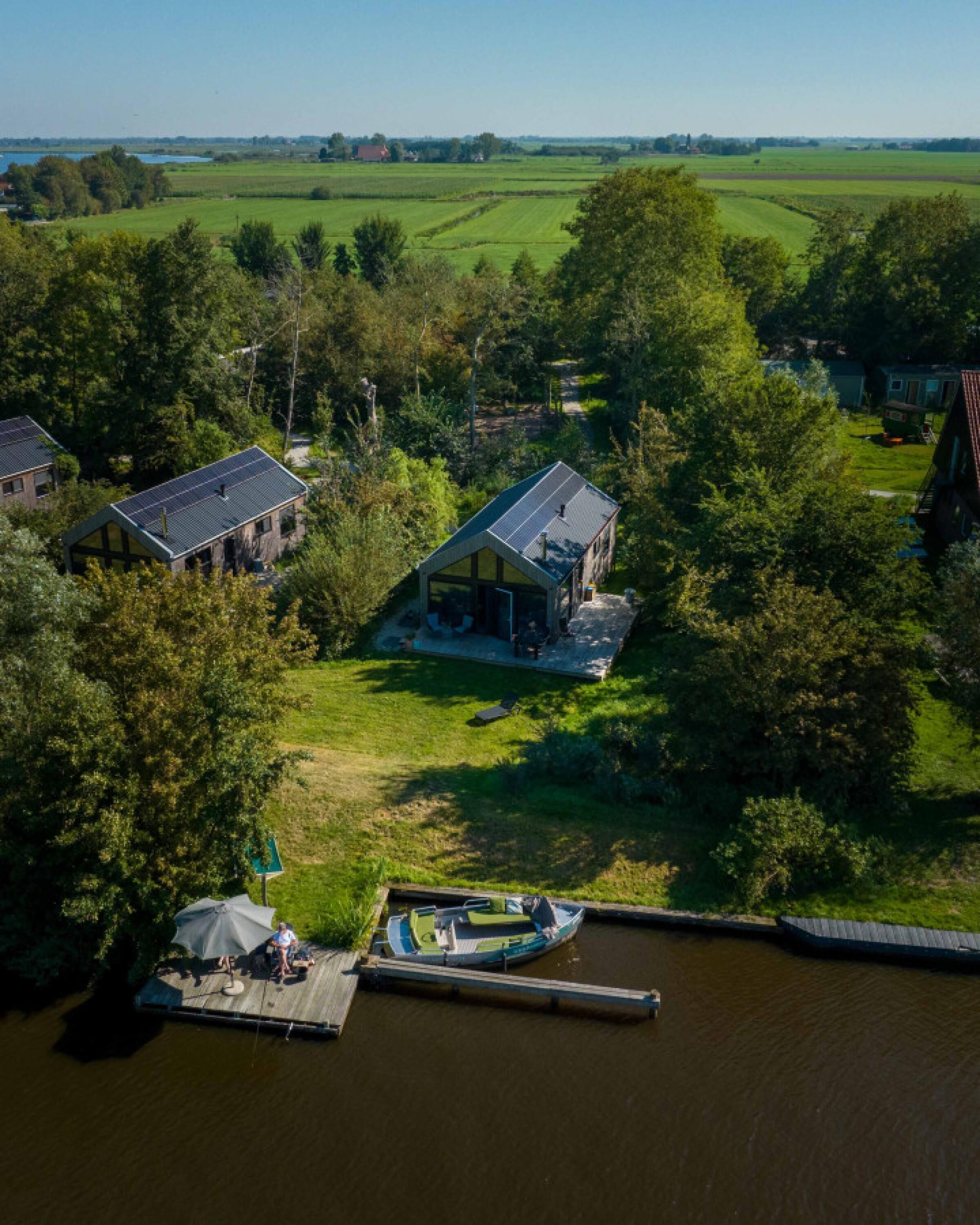 A riverside property with a dock, a boat, and two houses surrounded by greenery.