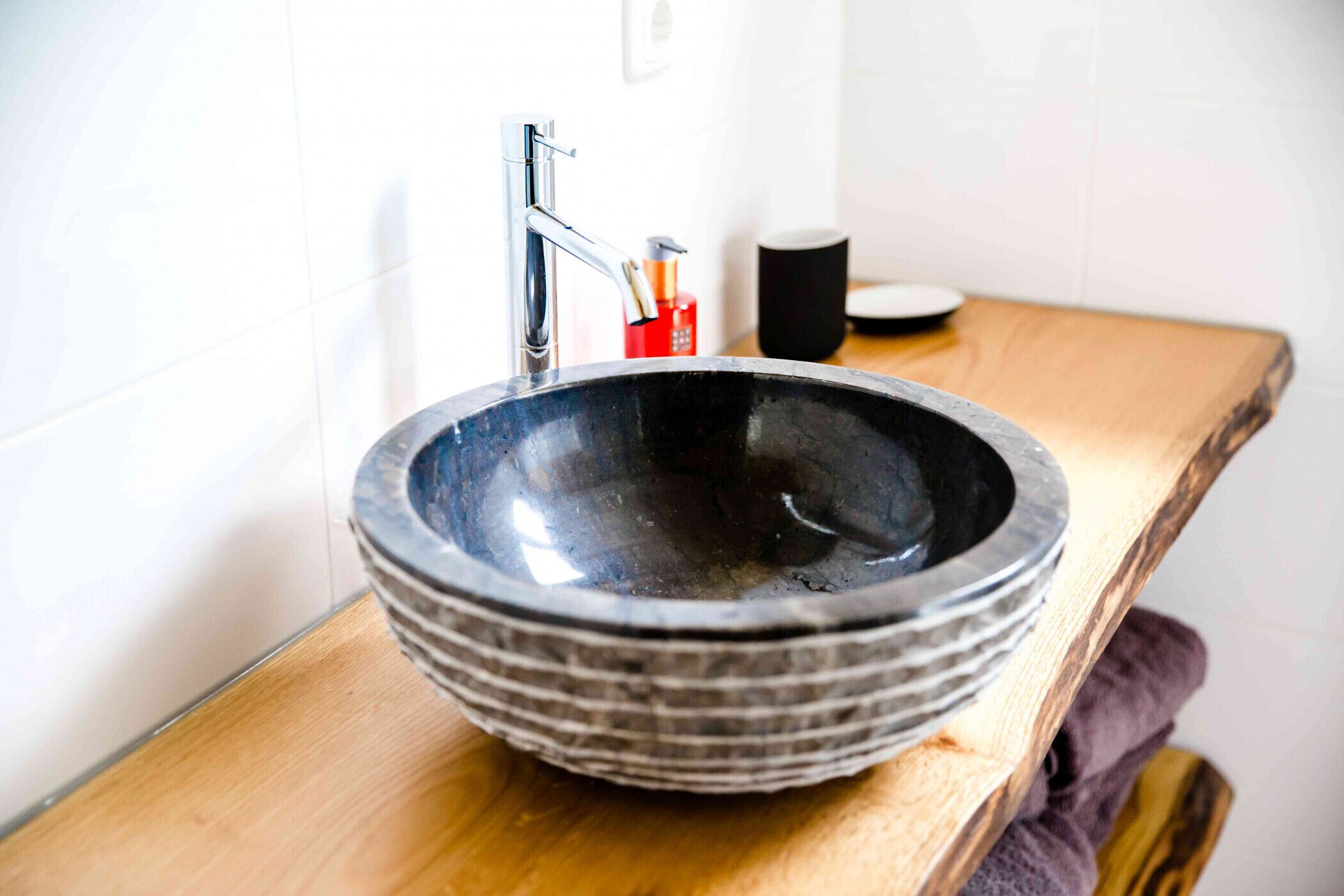 Un baño con un lavabo de cerámica grande y oscuro, un grifo moderno y una encimera de madera.