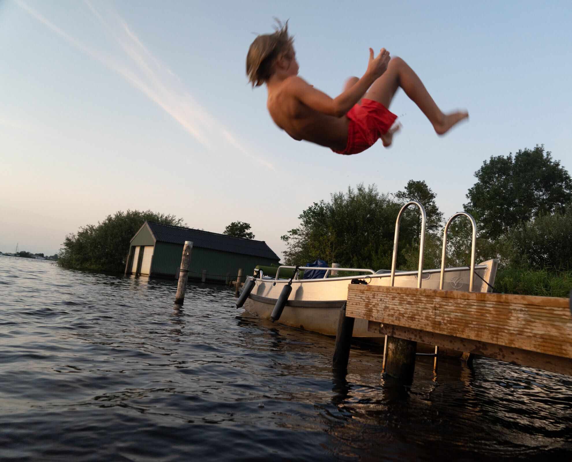 Eine Person springt von einem Steg ins Wasser.