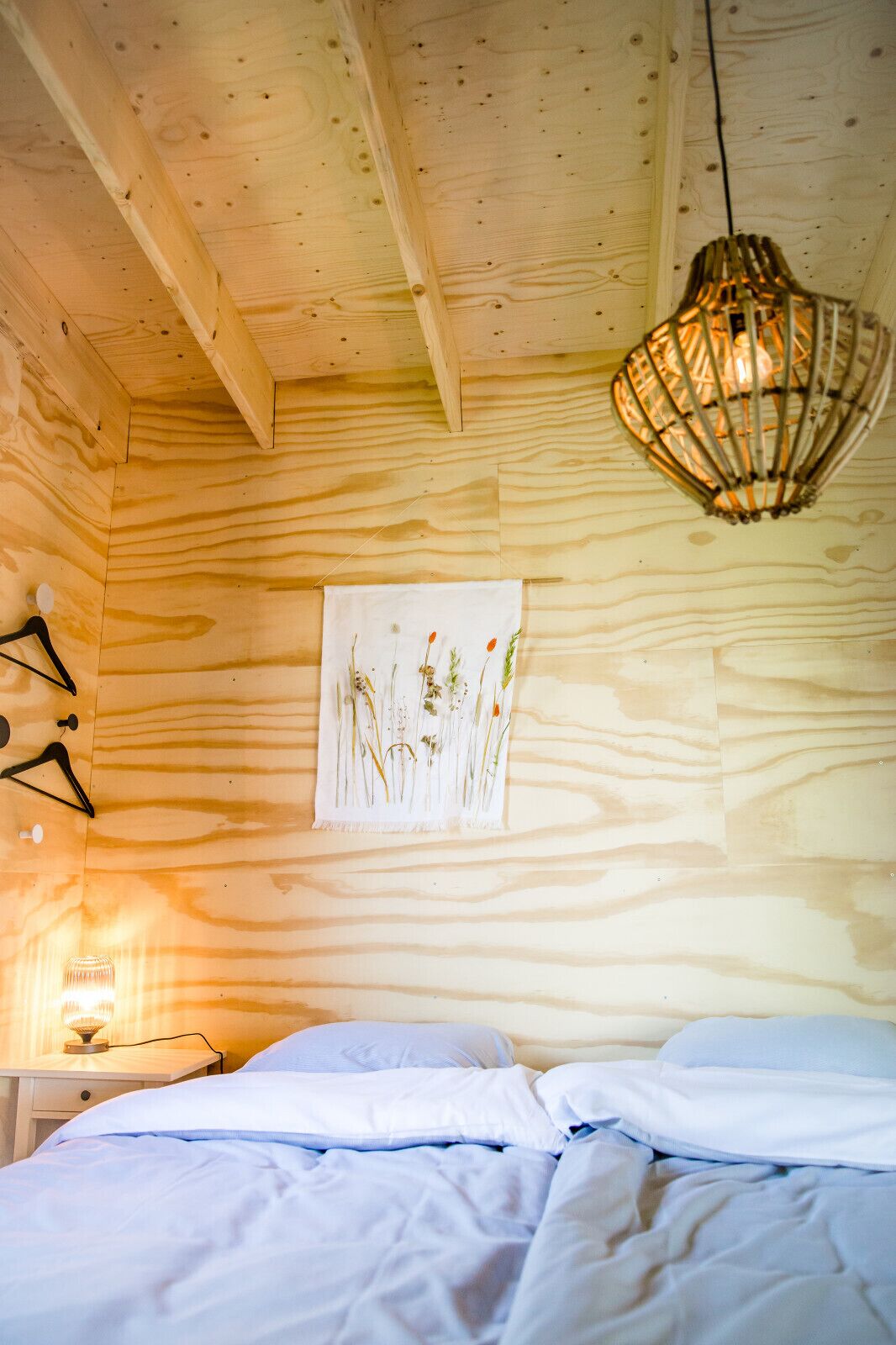 Una habitación de madera con una cama, una lámpara de pared y un cuadro con flores.