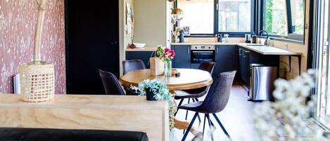 A modern interior with a wooden ceiling, a dining area with a round table, and a kitchen with large windows.