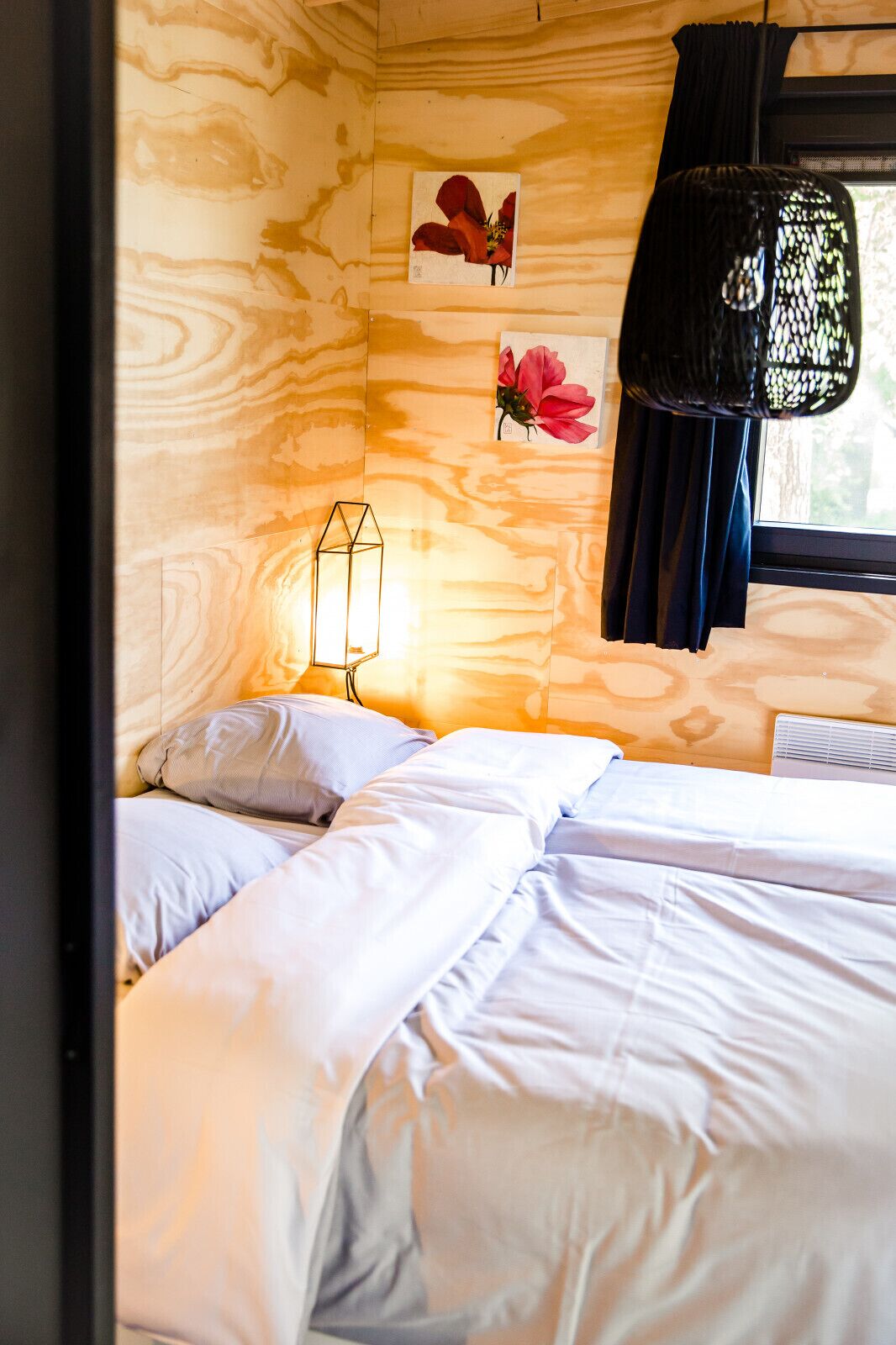 A bedroom with a wooden wall, a hanging chair, and two beds with white bedding.