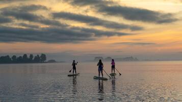 Drie personen paddleboarden op een kalm meer tijdens de zonsondergang.