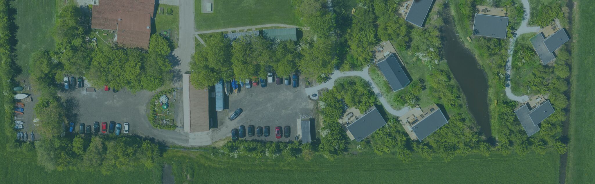 An aerial view of a residential area with multiple houses, a parking lot, and a river.