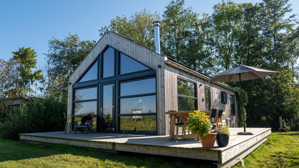 Una cabaña moderna de madera con ventanas de vidrio amplias, una terraza y una chimenea.
