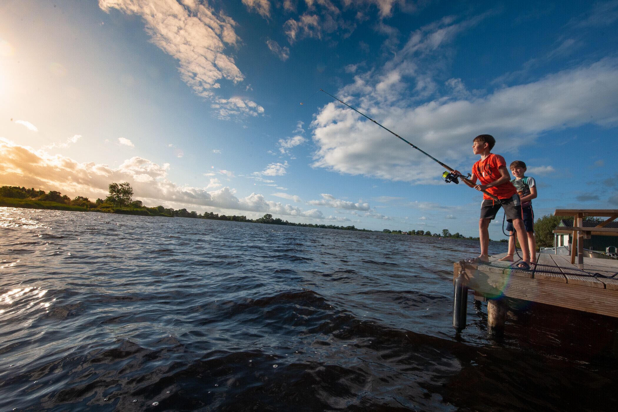 A wooden dock extending into a body of water with two individuals fishing.