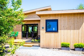 A modern wooden building with a large glass door entrance, outdoor seating, and potted plants. - Waterlodge Sweltsje in Nes (Nes)