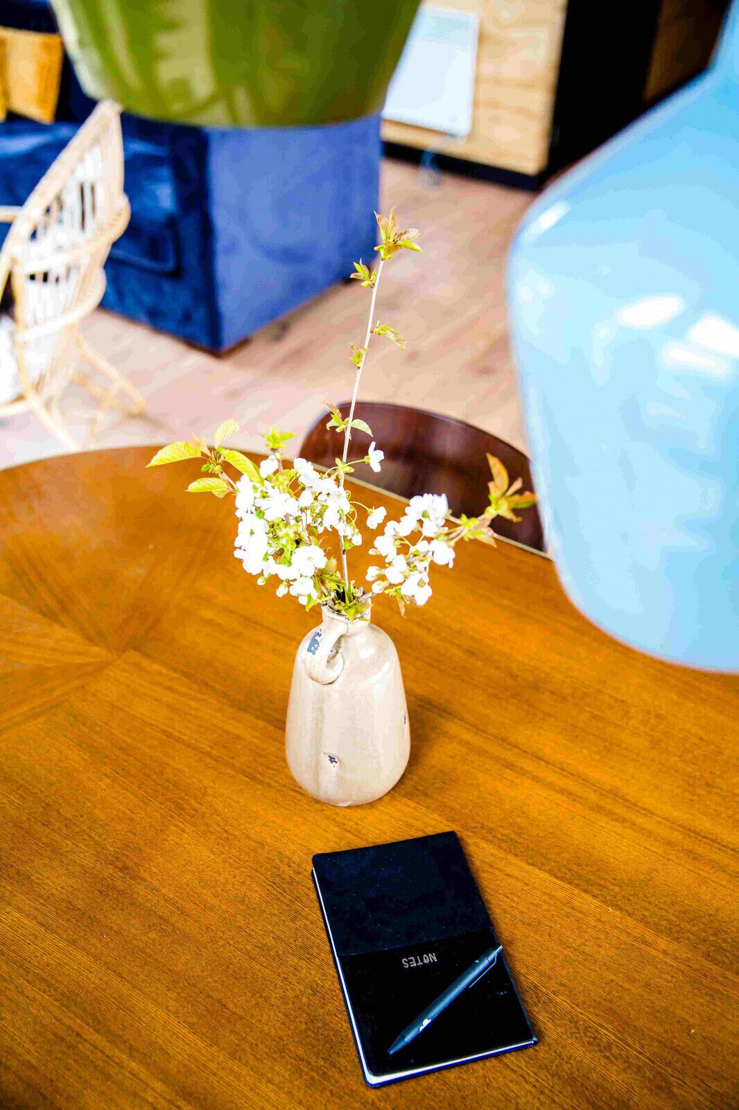 A wooden table with a ceramic vase containing white flowers and a smartphone.