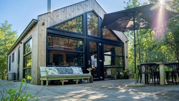 Een moderne houten hut met grote ramen en een overdekt terras.