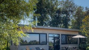 Una casa moderna con terraza, mobiliario exterior y un gran ventanal con vistas a un jardín.