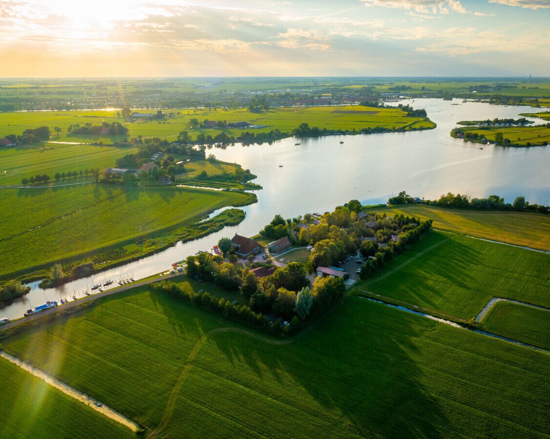 Una vista aerea di una proprietà lungo il fiume, con un gruppo centrale di edifici, circondata da campi verdi e un fiume calmo.