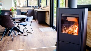 Una cocina moderna con estufa de leña, comedor con sillas y ventanas amplias.