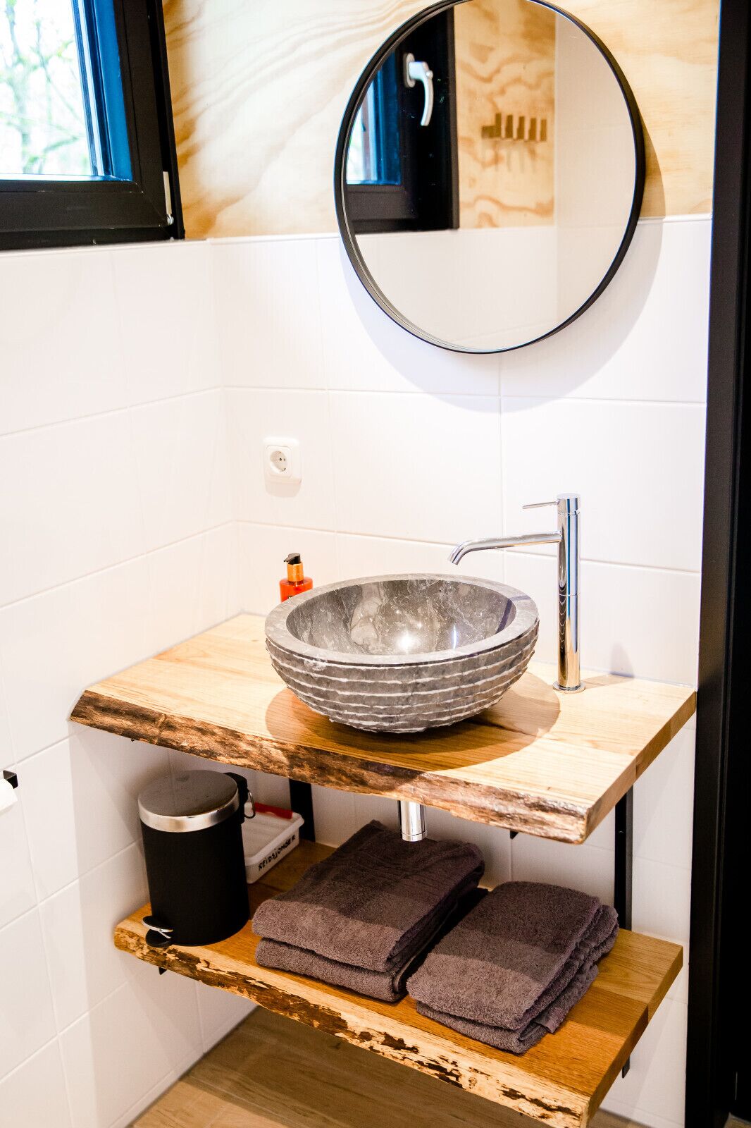 Een badkamer met een houten wastafelmeubel, een ronde spiegel, een wastafel en een handdoekrek.