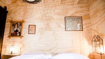 A wooden cabin room with a bed, a map, and a framed picture on the wall.