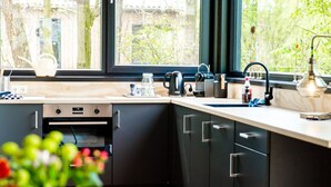 Una cocina moderna con armarios oscuros, horno empotrado, un lavabo y ventana con vistas a vegetación.