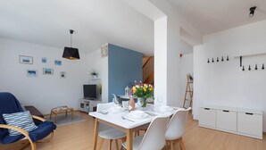 A modern living room with a dining area, wooden flooring, a blue accent wall, and a staircase leading to an upper level. - Spacious Family Suite | Balcony | 2 Bedrooms (Swinoujscie)