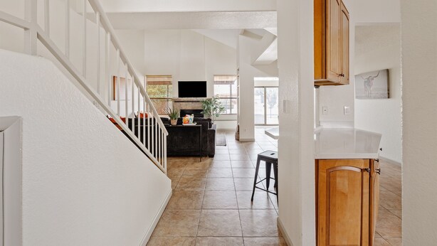 A spacious living area with a staircase, a flat-screen TV, and a dining area with a black sofa and a small table. - Lakefront Home | Community Pool & Hot Tub (Chandler)
