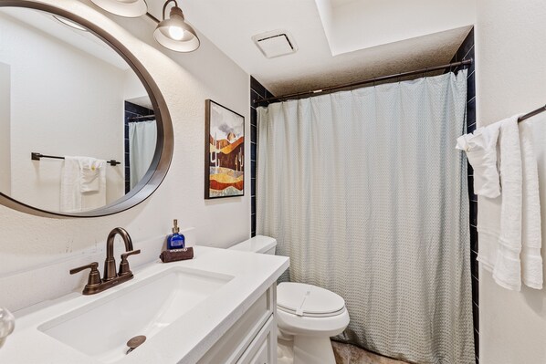 Une salle de bain avec un lavabo blanc, un miroir, des toilettes et un rideau de douche.