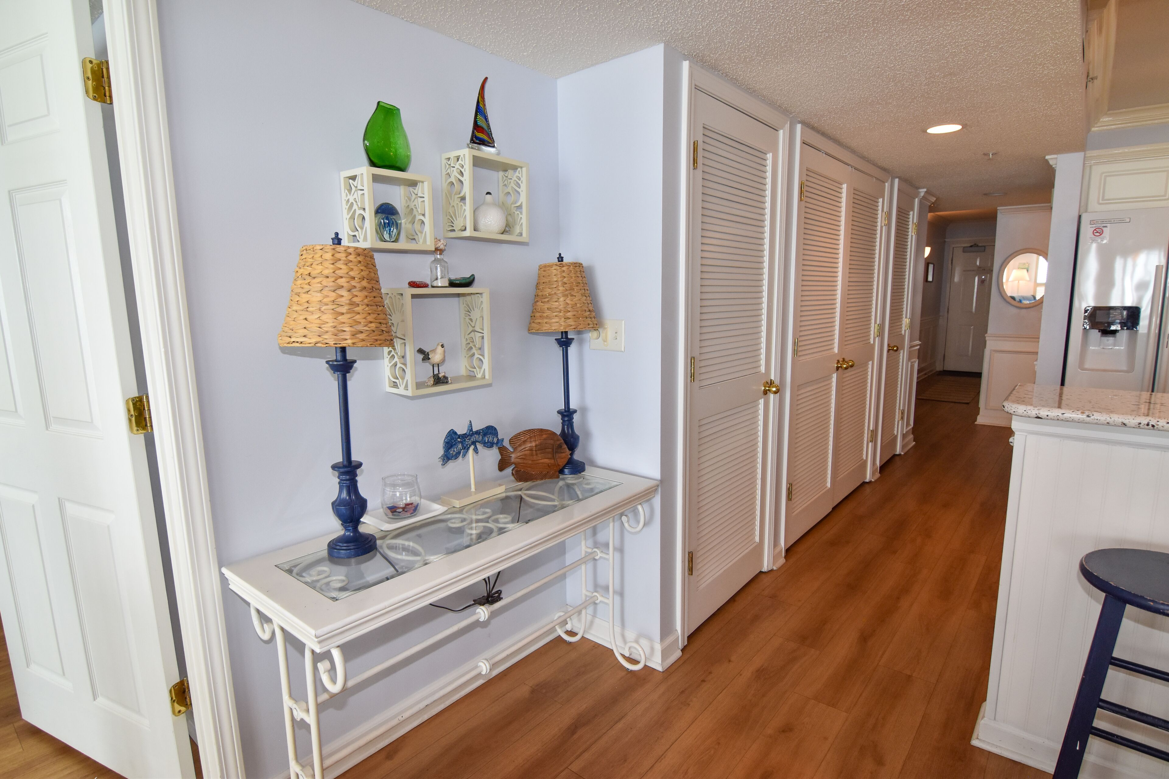 A hallway with a white console table, two lamps, and decorative items on shelves.