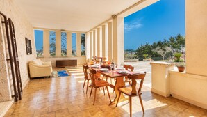 A spacious patio with a wooden table set for dining, large windows offering a view of the landscape, and a comfortable seating area. - 2845 Trulli Carvaloo by Barbarhouse (Martina Franca)