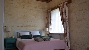 Un dormitorio con cama, dos mesitas de noche, una ventana con cortinas florales y techo de madera.