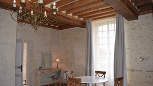 Un comedor con una mesa redonda, sillas de madera, una araña y una ventana con cortinas.