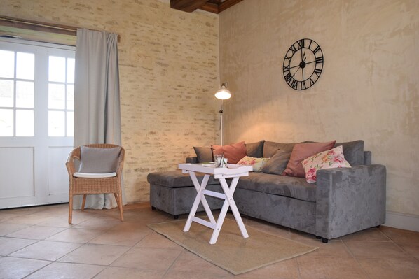 A cozy living room with a grey sofa, a wicker chair, a small white table, and a wall clock.