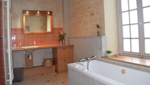 Un baño con bañera, lavamanos con espejo y ventana con marcos blancos, además de una planta en el alféizar.