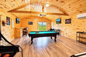 A wooden interior with a pool table, chairs, and a staircase.