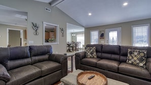 A spacious living room with two dark leather sofas, a wooden coffee table, and a dining area in the background.