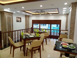 A dining area with wooden tables and chairs, a ceiling with recessed lighting, and a view of the outside through large windows.